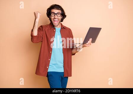 Photo portrait of cheerful guy celebrating holding laptop in hand isolated on pastel beige colored background Stock Photo