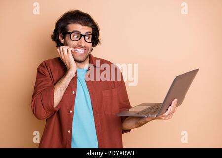 Photo portrait of scared man biting nails holding laptop in hand isolated on pastel beige colored background Stock Photo