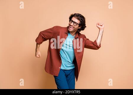 Photo of funny young man dance raise fists cheerful face wear eyeglasses brown t-shirt isolated beige color background Stock Photo