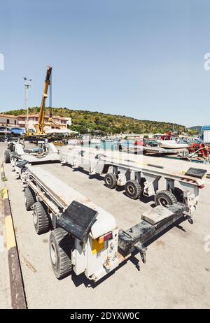 Yellow telescope crane truck and grey heavy-duty transporter for boats and yachts in the port of Talamone, Tuscany, Italy Stock Photo