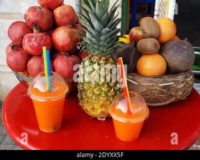 a plate of pomegranates, pineapple, tropical fruits and freshly squeezed juice in glasses. Stock Photo