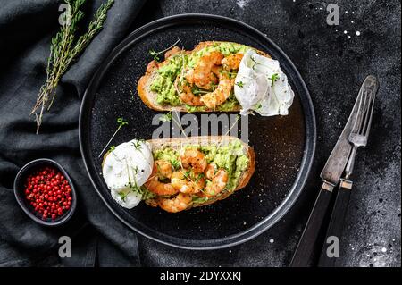 Bread with guacamole, fried shrimp, prawns and egg. Black background. Top view Stock Photo