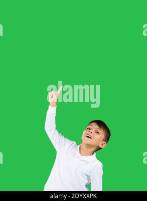 Caucasian toddler boy points up his index finger to an empty space where your advertisement may be. Green background. High quality photo Stock Photo