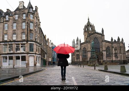 Woman holding red umbrella in rain on the Royal Mile in Old Town of Edinburgh, Scotland, UK Stock Photo
