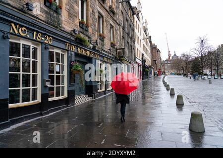 Woman holding red umbrella in rain in The Grassmarket in Old Town of Edinburgh, Scotland, UK Stock Photo