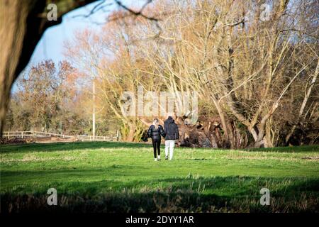 A landscape view of Letcombe Brook, East Hanney, Wantage, Oxfordshire, UK and surroundings with a young couple crossing a field  towards woodland. Stock Photo