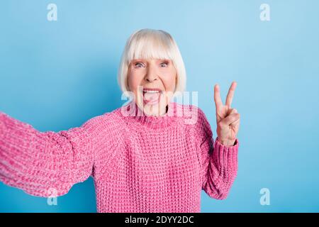Photo portrait of excited elderly woman showing v-sign taking selfie isolated on pastel blue colored background Stock Photo