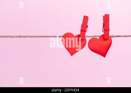 Two red hearts are hung on clips with place for text on a pink background. Valentine's day holidays and anniversary concept.
