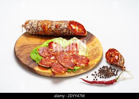 Cutting board with slices of spicy salami, black pepper and chilli. Stock Photo