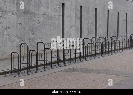 Long row of empty bike racks next to sidewalk near closed public school with bleak grey conrete wall during winter christmas school holidays Stock Photo