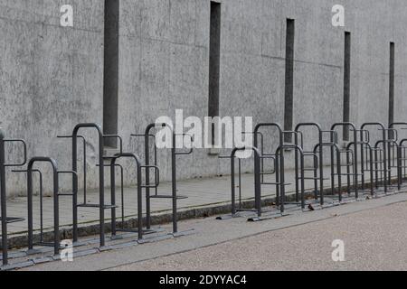 Long row of empty bike racks next to sidewalk near closed public school with bleak grey conrete wall during winter christmas school holidays Stock Photo