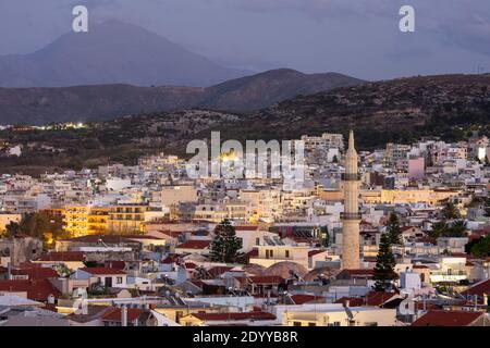 Cityscape view of Rethymno illuminated in the evening, as seen from Fortezza Castle, and showing the minaret of Neratze Mosque, Crete, Greece Stock Photo