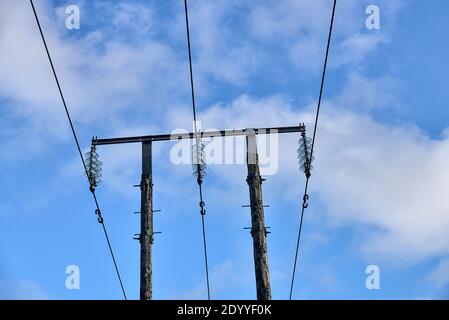 Overhead electrical power lines on old wooden pillar captured against the blue sky with soft white clouds in Co. Dublin, Ireland. Three voltage wires Stock Photo
