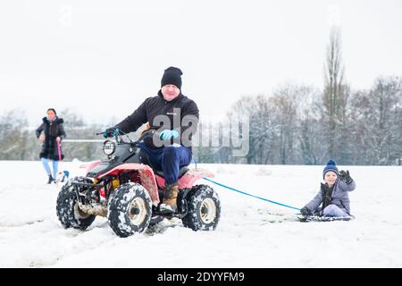 Kidderminster, UK. 28th December, 2020. UK weather: after a significant snowfall across Worcestershire this morning, families come up with novel ideas to entertain their children. Here we have a little boy being towed behind a quad bike while sitting aboard a dustbin lid! Credit: Lee Hudson/Alamy Live News Stock Photo