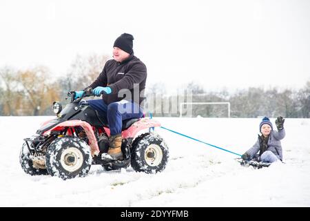 Kidderminster, UK. 28th December, 2020. UK weather: after a significant snowfall across Worcestershire this morning, families come up with novel ideas to entertain their children. Here we have a little boy being towed behind a quad bike while sitting aboard a dustbin lid! Credit: Lee Hudson/Alamy Live News Stock Photo