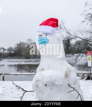 Kidderminster, UK. 28th December, 2020. UK weather: after significant snowfall across Worcestershire this morning, families start building tradtional snowmen, albeit with a slight difference due to Covid-19. This Christmas snowman is wearing a very obvious blue, protective mask - a touch of British humour to lift local spirits! Credit: Lee Hudson/Alamy Live News Stock Photo