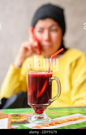 a glass goblet with mulled wine which includes senby red wine  and sliced orange with drinking straw stands on a table in a cafe against the backgro Stock Photo