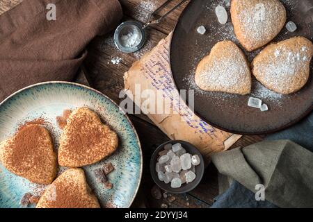 Heart-shaped cookies are sprinkled with cocoa and powdered sugar on a vintage background. Stock Photo