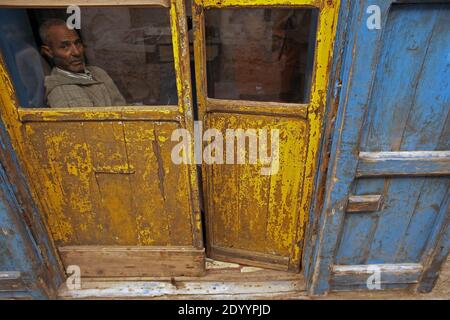 A man looks with curiosity through a yellow window  in the historic town or medina, Essaouira, Morocco, Stock Photo