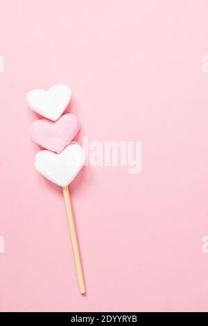 White and pink heart shaped marshmallows on a wooden stick on a pink background with copy space. Stock Photo