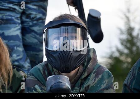 Paintball sport player girl in protective camouflage uniform and mask with marker gun outdoors Stock Photo
