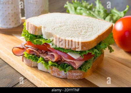 Fresh ham, tomato and cheese sandwich on cutting board Stock Photo
