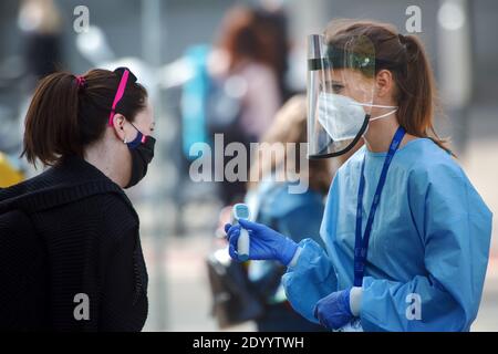 Young medic checking the temperature (with digital thermometer) of a woman waiting for a test of collective immunity against the corona virus. Stock Photo