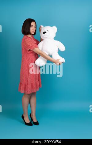 full-length portrait of a sad, upset, offended, angry woman pulling and tearing a white Teddy bear, a bad gift for Valentine's day Stock Photo