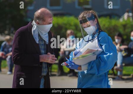 Medic with respirator and plastic face shield giving a questionnaire to a man with cloth face mask before undergoing a corona virus test. Stock Photo