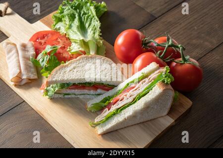 Fresh turkey, lettuce and tomato sandwich cut in half on cutting board Stock Photo