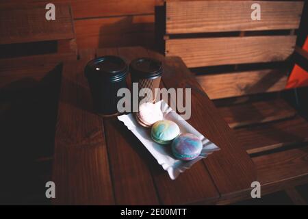 Two single use disposable cups with coffee and macarons on the wooden table otside outdoors cozy atmosphere Stock Photo