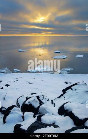 Snow covering rocky shore. Lake water starts to freeze on a cold winter day. Stock Photo
