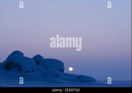 Winter landscape at dusk. Sun setting behind snow covered boulders. Stock Photo