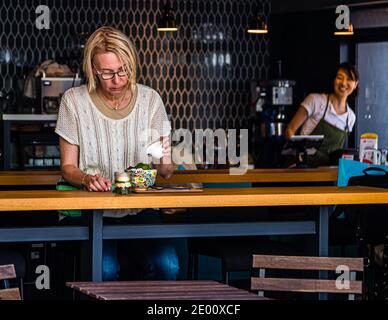 A tourist drizzles syrup over her kakigori (Japanese shaved ice) topped with green matcha at a café in Shizuoka, Shizuoka Prefecture, Japan. Green tea meets visitors of the "City of Green Tea" in many variations – on ice cream, in layered pudding, in pastries or straight on the rocks. A stroll through Shizuoka is worth it to learn more about green tea. Stock Photo