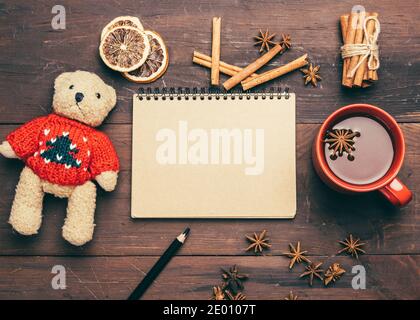 red ceramic cup with cocoa, notepad with blank sheets and brown teddy bear toy on a wooden table, top view Stock Photo