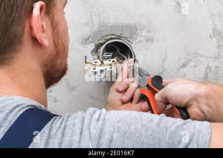 A man dismantles and mends an electrical outlet for repairs. Power socket. Stock Photo