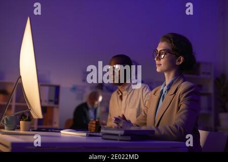 Group of multi-ethnic office workers doing their job in evening using computers in dark room, copy space Stock Photo