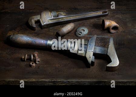 Old pipe wrenches, nuts and bolts, pipes, fittings, and washers on old wooden table Stock Photo