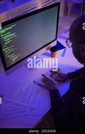 Vertical high angle view shot of unrecognizable man working on computer code late in evening in dark office room Stock Photo