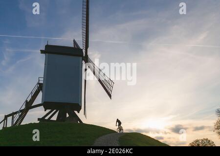 A cyclist rides by a traditional windmills in Park Kruisvest on a sunny autumn day in Bruges, Belgium Stock Photo