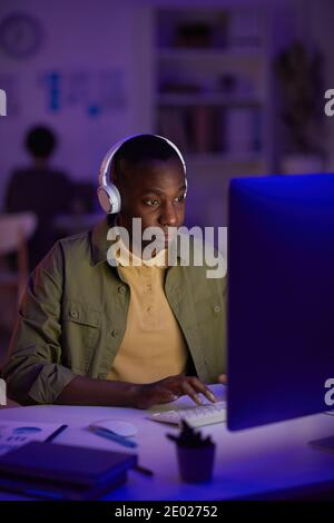 Portrait of African American man wearing casual outfit listening to music in headphones while working on computer in evening Stock Photo