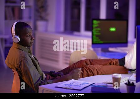 Young adult African American man wearing headphones sitting relaxed in office room working in evening Stock Photo