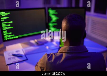Rear view shot of unrecognizable African American computer programmer sitting in front of monitors working on software code Stock Photo