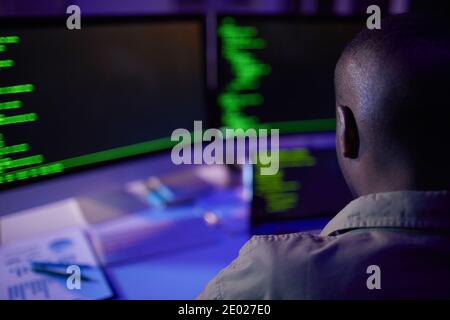 Unrecognizable African American soft developer sitting at desk in front of computers working on new code, rear view shot Stock Photo
