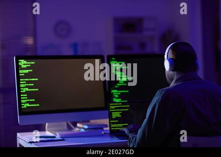 Rear view shot of professional software developer wearing headphone sitting alone in office working on computers making new code Stock Photo