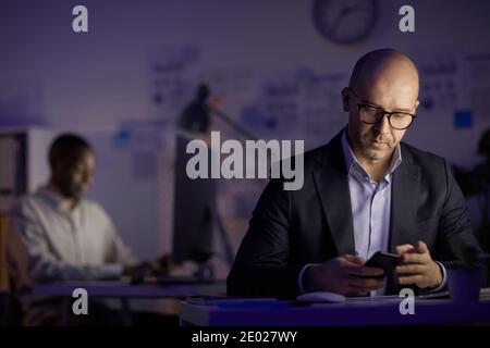 Handsome mature man wearing eyeglasses finishing workday in evening checking e-mail on smart phone, copy space Stock Photo