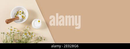 White cosmetic jar of cream, bouquet of chamomile flowers and mortar bowl with pestle on beige, brown background. Concept natural herbal organic cosme Stock Photo
