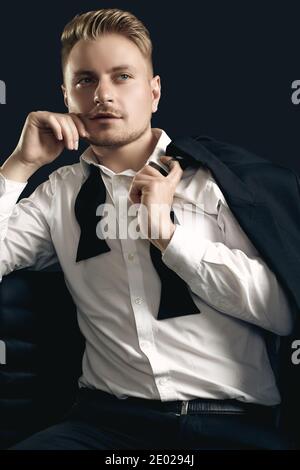 Portrait of handsome blond man in elegant tuxedo and bow tie posing on black studio background Stock Photo