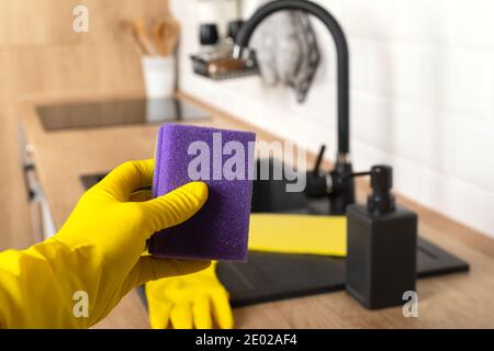 Housekeepers hand holding cleaning supplies in front of black kitchen sink Stock Photo