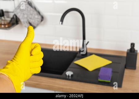 Housekeepers hand holding cleaning supplies in front of black kitchen sink Stock Photo